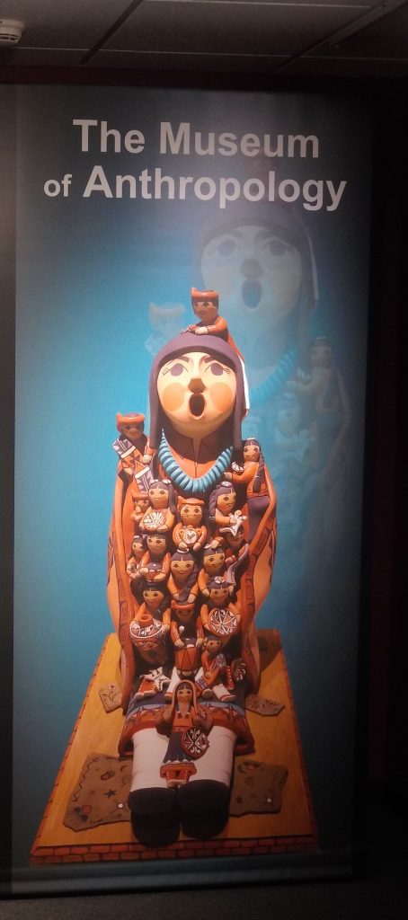 A figurine with many other figurines on it. The words The Museum of Anthropology written across the top.