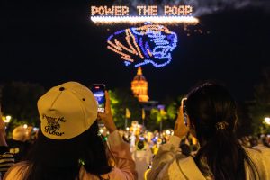Students photograph a drone show that says Power the Roar