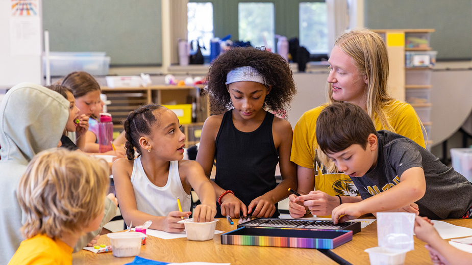 Adventure Club children at a table with a Mizzou student site facilitator