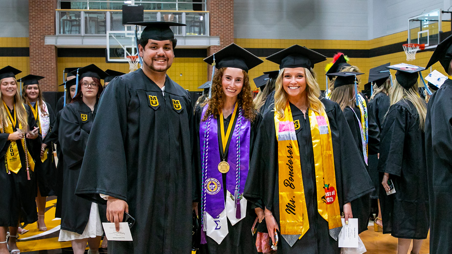Three students in caps and gowns at graduation