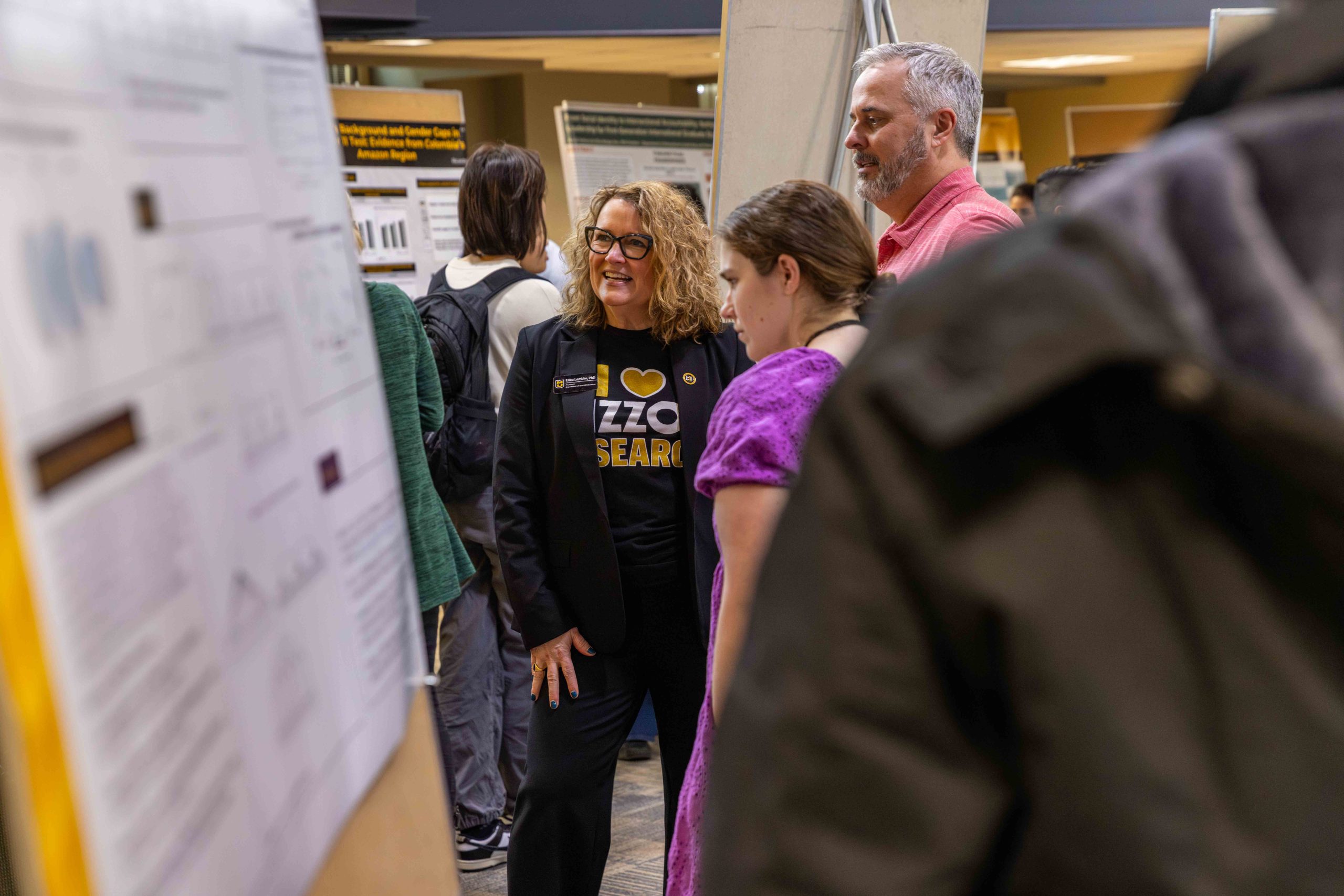 smiling woman standing in front a poster board with two other people