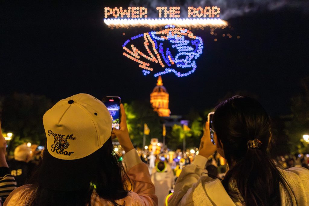 Students photographing a drone show that says Power the Roar